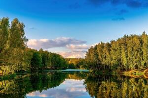 Sunset or dawn on a pond with birch trees along the banks and a cloudy sky reflected in the water. photo