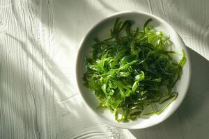 Top view to a plate with green salad made from chukka seaweed on a wooden table, illuminated by bright sunlight. Vegan seafood. photo