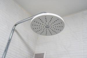Shower head made of white plastic with a metal pipe on the background of a wall in the bathroom. photo