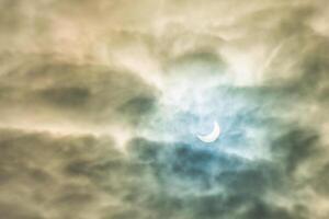 Partial solar eclipse passing behind the clouds. photo