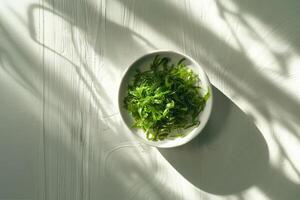 Top view to a plate with green salad made from chukka seaweed on a wooden table, illuminated by bright sunlight. Vegan seafood. photo