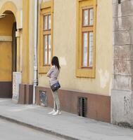 Timisoara, Rumania - abril 13, 2014 - mujer vistiendo un negro bolso es esperando cerca un amarillo edificio en el calle foto