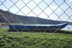 Empty wooden boat at the lake. View trough a wire fence photo