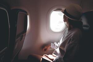 Woman looks out the window of an flying airplane. Young caucasian happy passengers are traveling by plane, watching the sky from above and hold passport photo