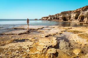 Tourist woman stand on rocky formations by sea cave in Ayia Napa, Cyprus. A shot from the inside of a sea cave in sunny Mediterranean coast of greek Cyprus. Grotto sea cave swim photo