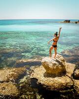 Young beautiful woman tourist stand on viewpoint rock enjoying sun and turquoise sea background near Ayia Napa of Cyprus coast photo