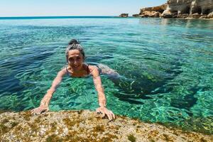 Tourist swim in Northern cyprus Ayia napa bay shore with crystal clear blue mediterranean waters and tranquil seascape and rocky stone shore. Sea caves popular travel destination photo