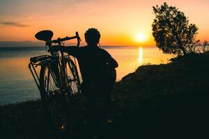 Silhouette of cyclist traveler with his bicycle enjoy sunset view together by tranquil Sevan lake in nature. Bicycle touring outdoors in nature photo