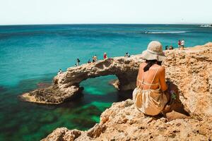 Woman tourist sit on viewpoint sightseeing Cyprus greek island visit stone arch or bridge of Love. Famous holiday destination in mediterranean seacoast photo