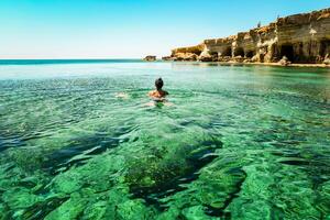 turista nadar en del Norte Chipre ayia napa bahía apuntalar con cristal claro azul Mediterráneo aguas y tranquilo marina y rocoso Roca costa. mar cuevas popular viaje destino foto