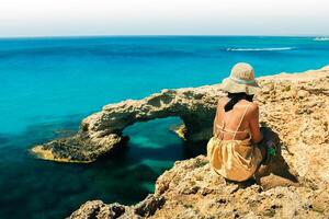 Woman tourist sit on viewpoint sightseeing Cyprus greek island visit stone arch or bridge of Love. Famous holiday destination in mediterranean seacoast photo