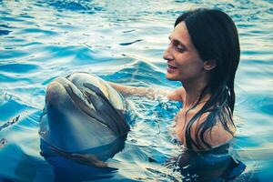 Portrait of young Caucasian woman smile with dolphin look to camera in pool water of Batumi delphinarium. Swim with dolphin experience concept photo