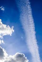 Aircraft condensation contrails in the blue sky inbetween some clouds photo