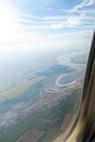 Land view through the airplane window. Fields, roads, rivers from a bird's eye view. Porthole. Look out the window of a flying plane. Top view of the ground photo