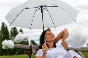 woman is holding a white umbrella and surrounded by cotton clouds photo