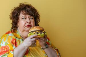 Elderly woman enjoying tasty burger on soft toned background with space for text photo