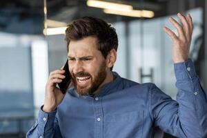 Frustrated male executive having a heated conversation on a smartphone in a modern office environment. photo