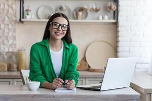 Young woman takes notes in front of laptop at home. Working from home. photo