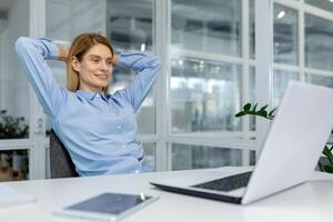 A professional woman takes a moment to relax in her bright office, exuding calmness and confidence behind her laptop. photo