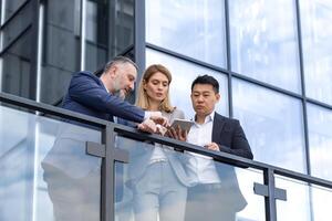 Specialist IT team leaders, group of business people outside office building, discussing and talking, testing new app on tablet, professional colleagues in business clothes, photo