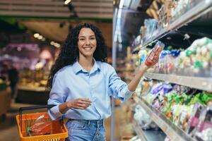 retrato de hermosa vegetariano mujer en supermercado, latín americano mujer elige vegetales para cena, sonriente y mirando a cámara foto