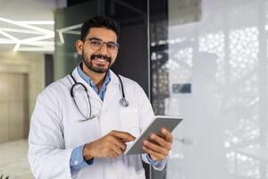 confidente masculino médico sonriente y participación un tableta en moderno hospital ambiente foto