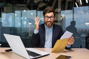 Portrait of happy mature investor businessman in office, man looking at camera and shocked happy and smiling, boss opening envelope with good news notification. photo