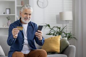 alegre maduro hombre participación crédito tarjeta y utilizando teléfono inteligente a tienda en línea desde el comodidad de su hogar. foto