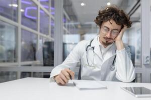 un médico en un blanco Saco se sienta a un mesa con un estetoscopio en su mano. foto