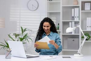 un alegre Hispano mujer trabajos desde un bien organizado hogar oficina, exudando profesionalismo y contentamiento como ella manejas documentos. foto