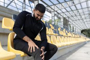 enfocado atleta tomando un descanso desde capacitación, extensión su pierna en amarillo estadio asientos con un contemplativo expresión. foto