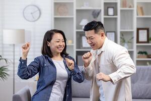 contento asiático Pareja hombre y mujer bailando juntos a hogar en tiempo de día en vivo habitación, contento joven familia celebrando contento día y Boda aniversario. foto