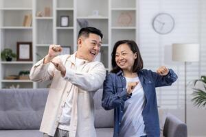 contento asiático Pareja hombre y mujer bailando juntos a hogar en tiempo de día en vivo habitación, contento joven familia celebrando contento día y Boda aniversario. foto