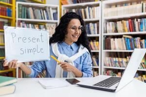 Enthusiastic online English teacher holding a whiteboard, explaining grammar in a virtual class amidst a bookshelf backdrop. photo