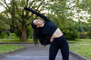 Joyful woman practicing side stretch in a tranquil park setting, embodying health and wellness during an outdoor workout. photo