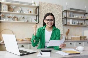 Happy woman in glasses and green shirt at home doing paper work got good result photo