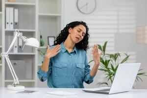 An overworked businesswoman is fanning herself, showing signs of heat and discomfort in a brightly lit office setting. photo