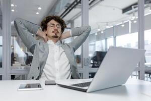 adulto masculino oficina trabajador a su escritorio toma un momento a relajarse, exhibiendo relajación y un contenido emocional estado en medio de un ocupado trabajo ambiente. foto