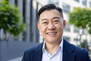 Mature Asian man in business attire smiles confidently in an urban outdoor setting, conveying success and positivity. photo
