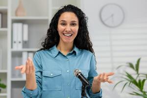 A professional woman gestures during a webcam meeting, as seen from the camera's point of view in a bright office setting. photo