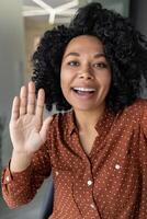 Vertical shot, young beautiful african american business woman with curly hair talking on call, waving at smartphone camera, using remote communication app photo