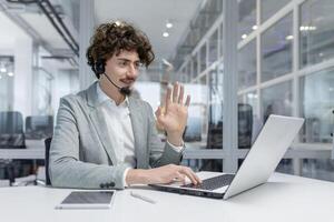 Focused young adult businessman sporting headphones in a lively call at his workplace, exuding professionalism and engagement. photo