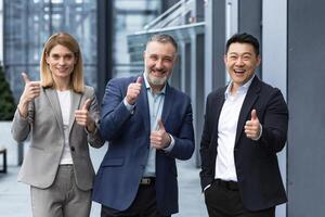 alegre sueño equipo, mayor y experimentado eso profesionales en negocio trajes sonriente y contento participación pulgar arriba y mirando a cámara, diverso grupo de proyecto gerentes fuera de oficina edificio. foto