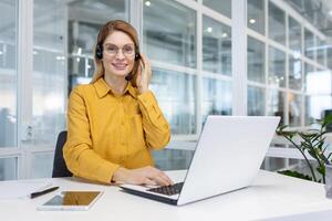 retrato mujer de negocios, oficina trabajador mirando a cámara y sonriente, utilizando auriculares y ordenador portátil para remoto en línea comunicación, cliente apoyo tecnología llamada centrar trabajador foto