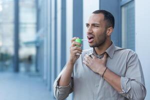 A young Latin American man clears his throat with an inhaler and medication. He stands outside photo