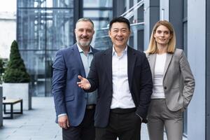 Successful diverse business team, three workers smiling and looking at camera, dream team with asian boss outside office building, colleagues in business suits photo