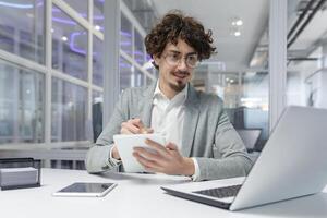 profesional joven masculino con Rizado pelo trabajando a ordenador portátil en un corporativo oficina configuración, demostración atención y pericia. foto