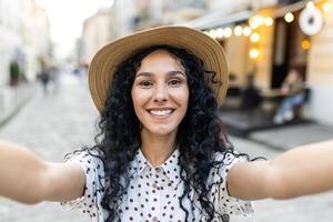 joven hermosa latín americano mujer caminando en noche ciudad, mujer mirando dentro teléfono inteligente cámara, utilizando llamada aplicación, hablando con amigos sonriente. foto