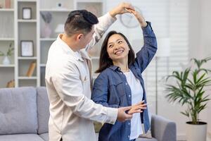 contento asiático pareja, joven familia hombre y mujer celebrar Moviente a un nuevo casa, comprando un departamento. ellos bailar, abrazo, reír. foto