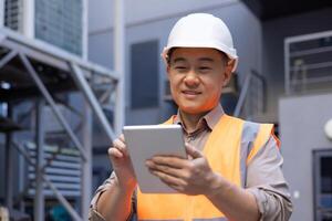 A smiling Asian man is working on a construction site. foreman, foreman. Standing outside and using a tablet. Close-up photo. photo